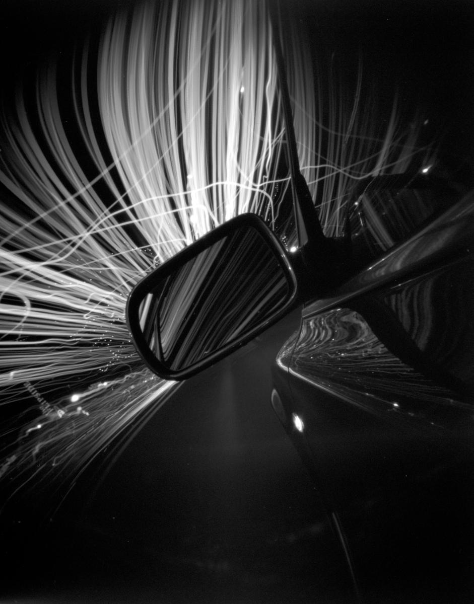 A car mirror reflects light trails from a long exposure photograph.