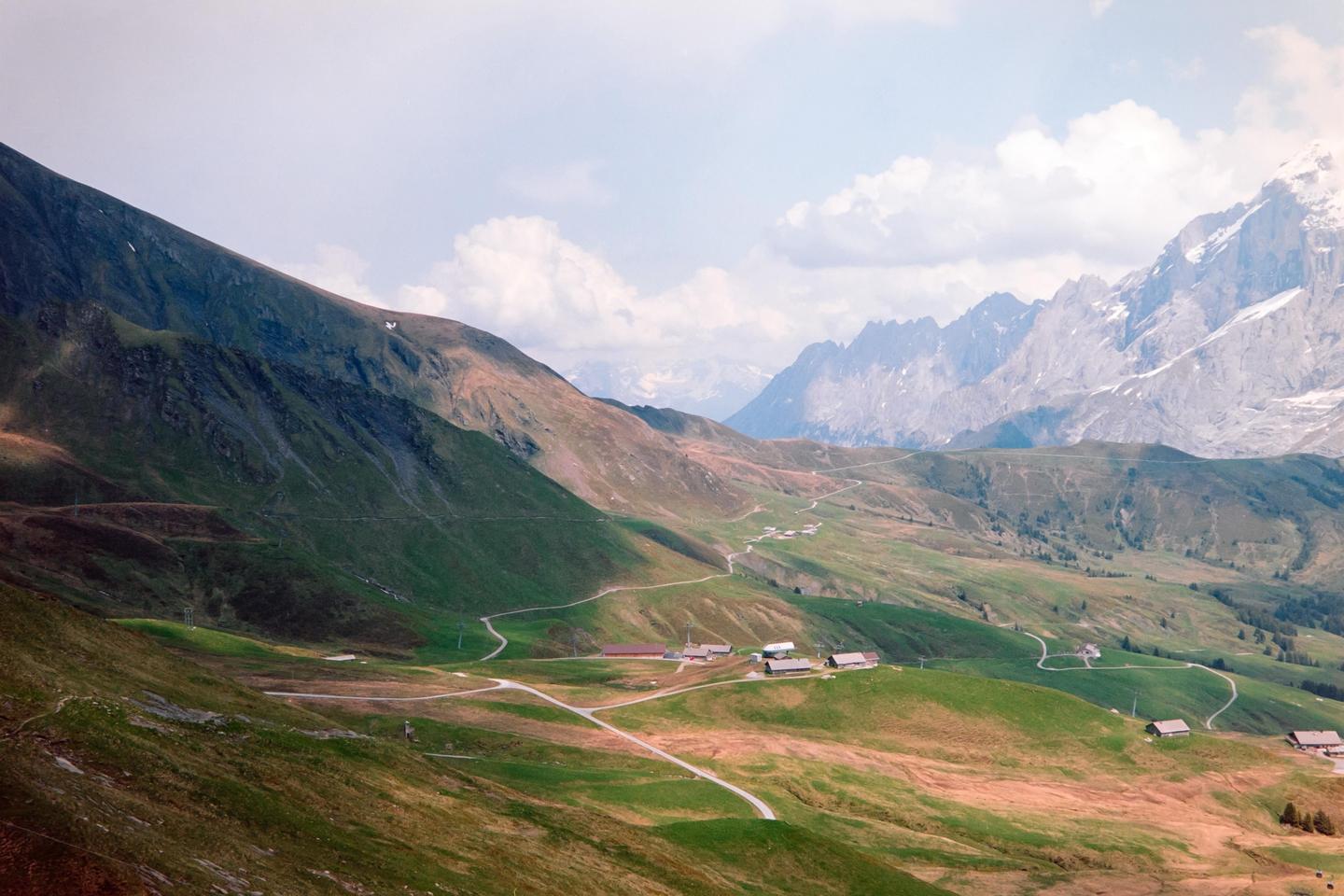 A winding road leads through a green valley with mountains in the background.