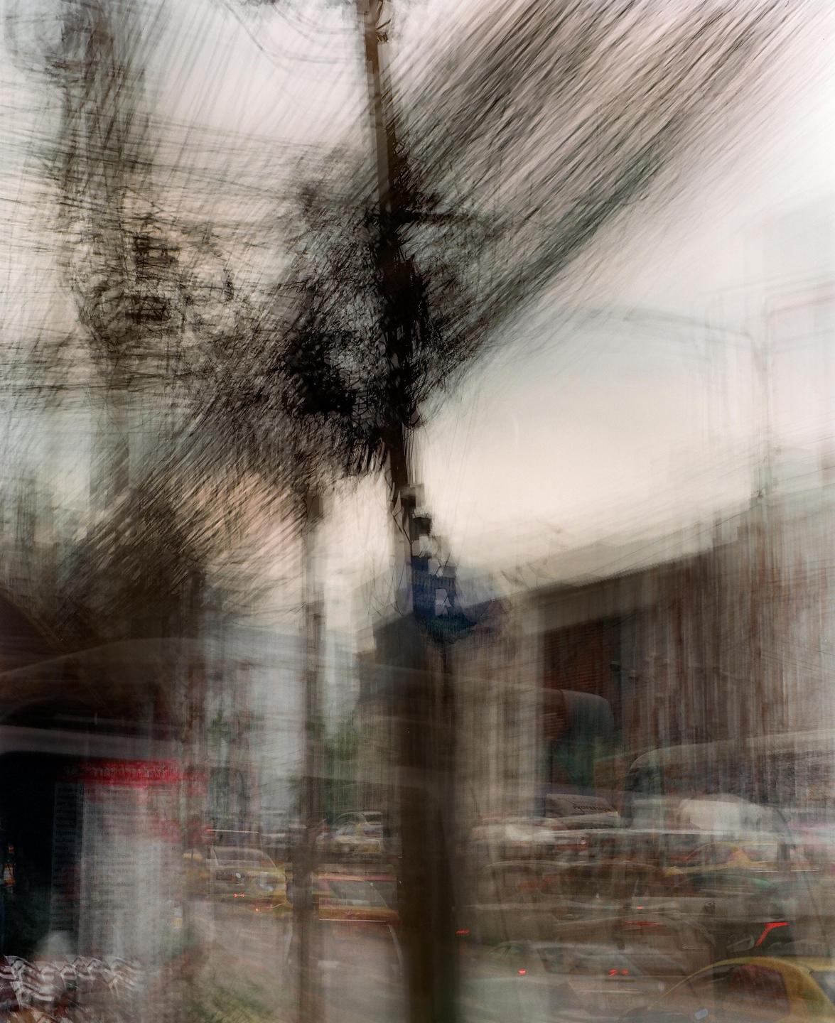 A blurred street scene shows a utility pole and tree branches against a light sky, with indistinct vehicles and buildings in the background.