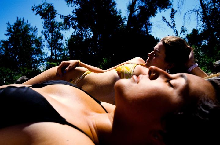 Two women in swimsuits are lying down under a bright blue sky with trees in the background.