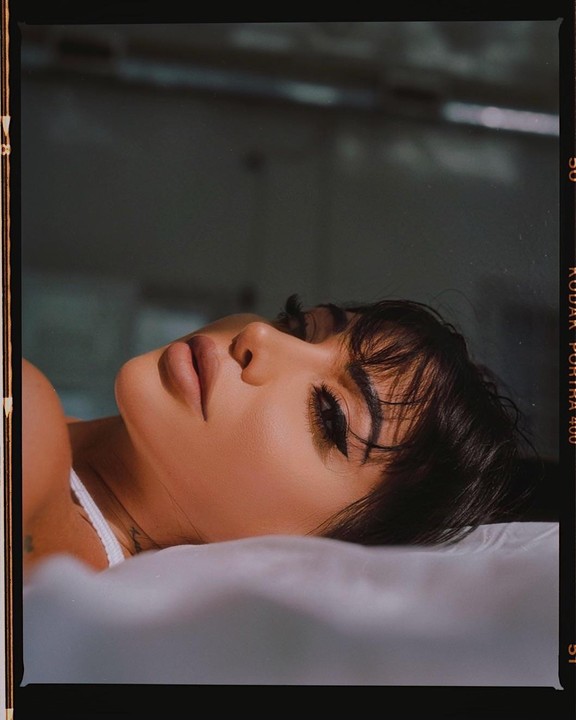 A woman with dark hair and makeup is lying on a white pillow, looking up.