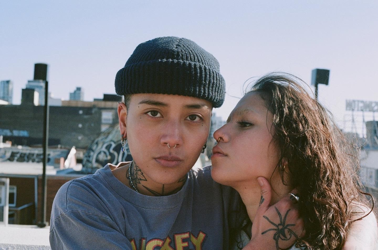 A couple poses for a portrait on a rooftop with a city skyline in the background.