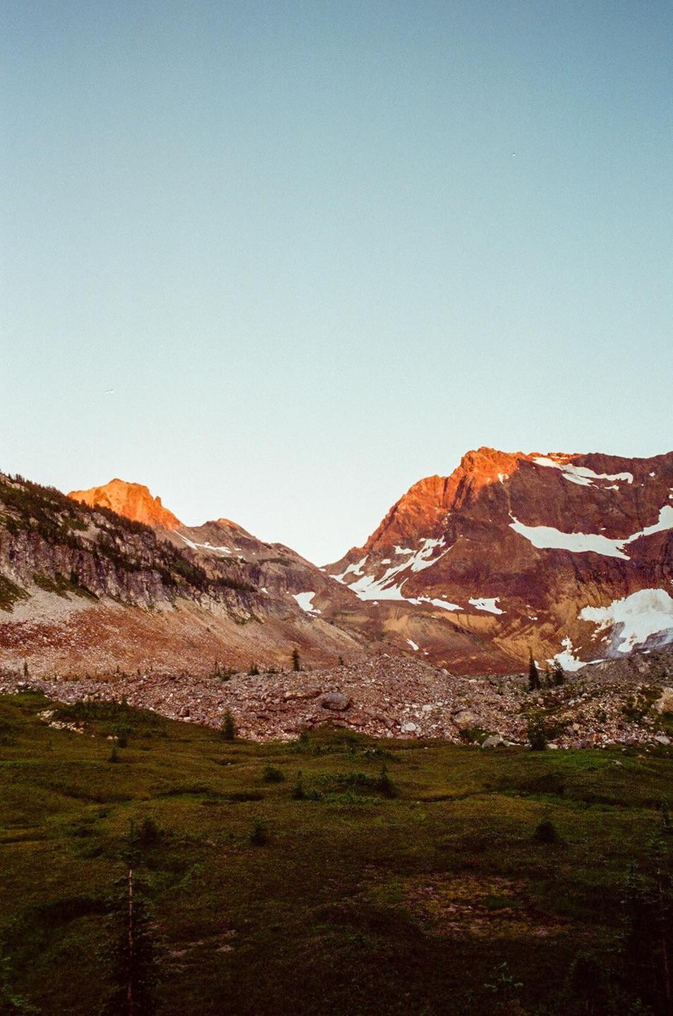 A mountain range with snow-capped peaks and a green valley is illuminated by the golden hour light.