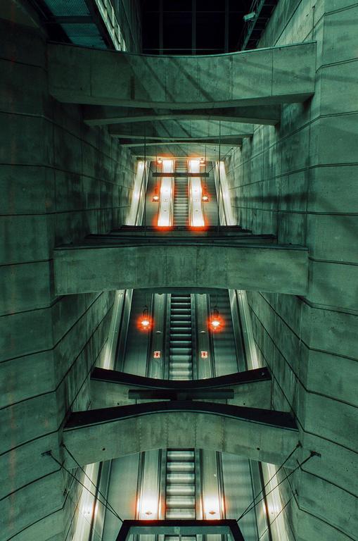 A long exposure shows multiple escalators with glowing red lights in a concrete building.