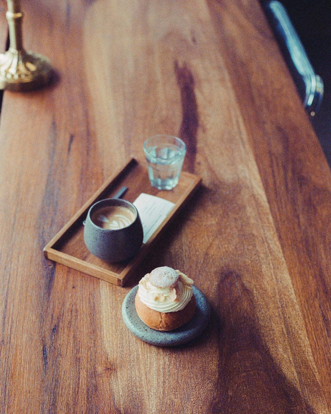 A coffee, a glass of water, and a pastry are arranged on a wooden table.