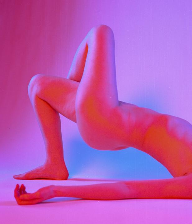 A body is posed on a surface with pink and blue light.