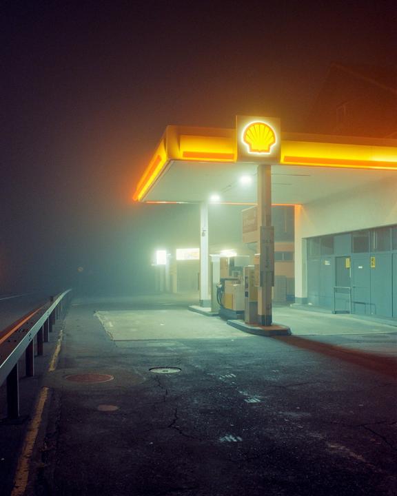 A Shell gas station with illuminated signage stands in a hazy night.