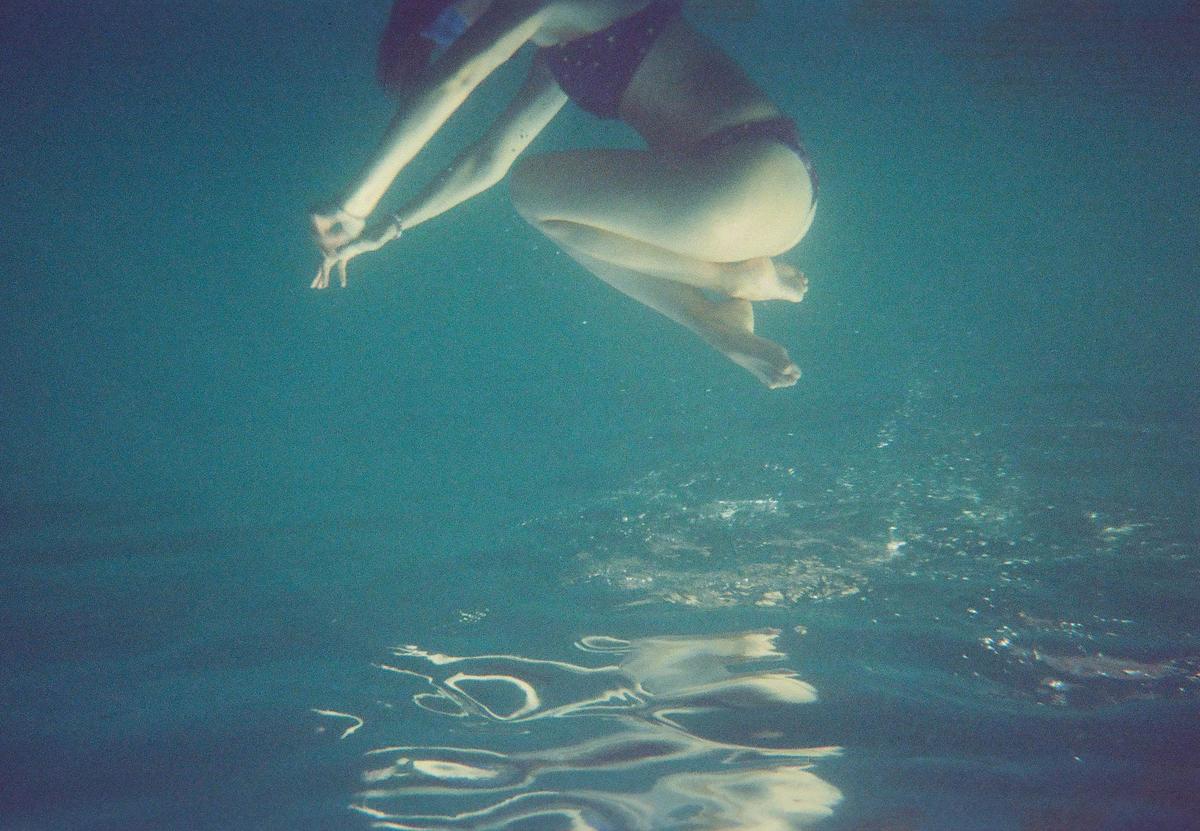 A woman in a bikini floats underwater with her arms extended and knees bent.