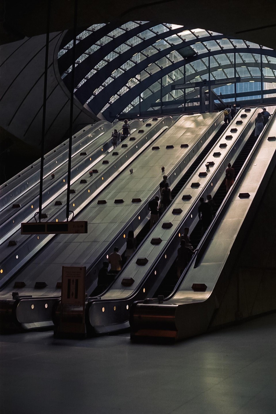 People ride multiple escalators under a glass and metal arched ceiling.