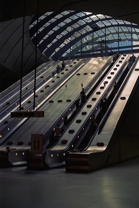 People ride multiple escalators under a glass and metal arched ceiling.