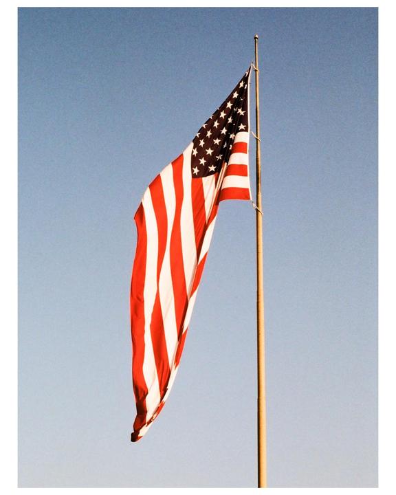 An American flag hangs from a flagpole against a clear sky.