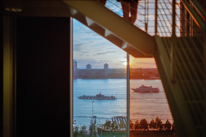 Two boats are on the water with a city skyline in the background, viewed through a window and staircase.
