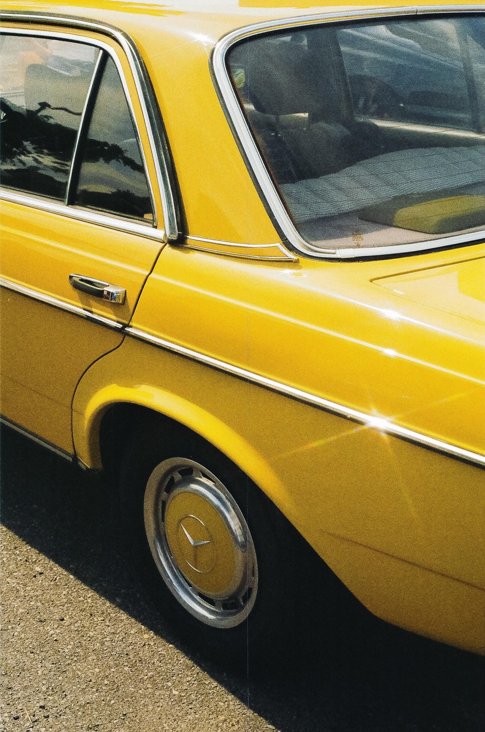 A yellow car with chrome trim is parked on an asphalt surface.