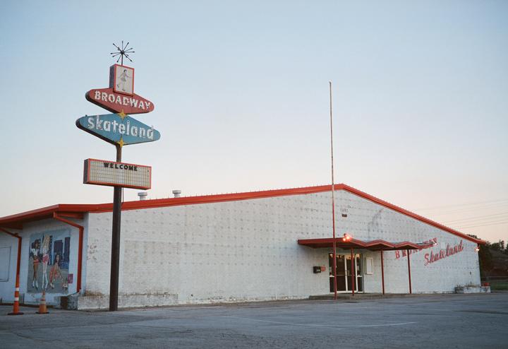 A vintage sign for Broadway Skateland stands in front of a white building with a red roof.