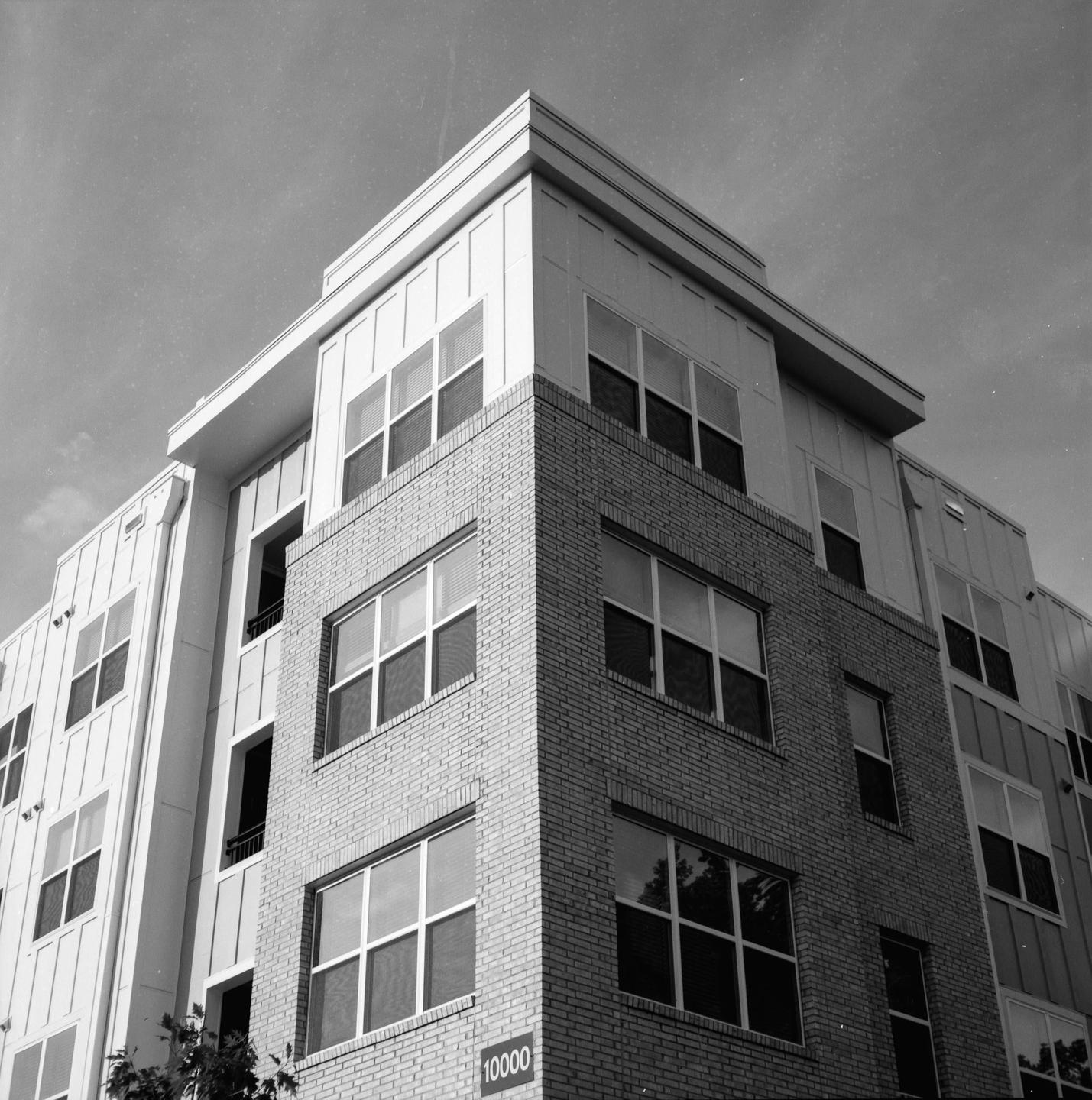 A modern building with brick and white siding is shown from a low angle against a clear sky.