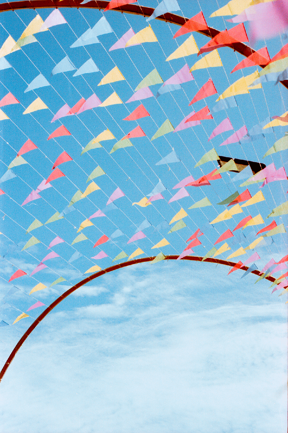 Colorful triangular flags are strung across a bright blue sky, with a brown arch visible at the bottom.