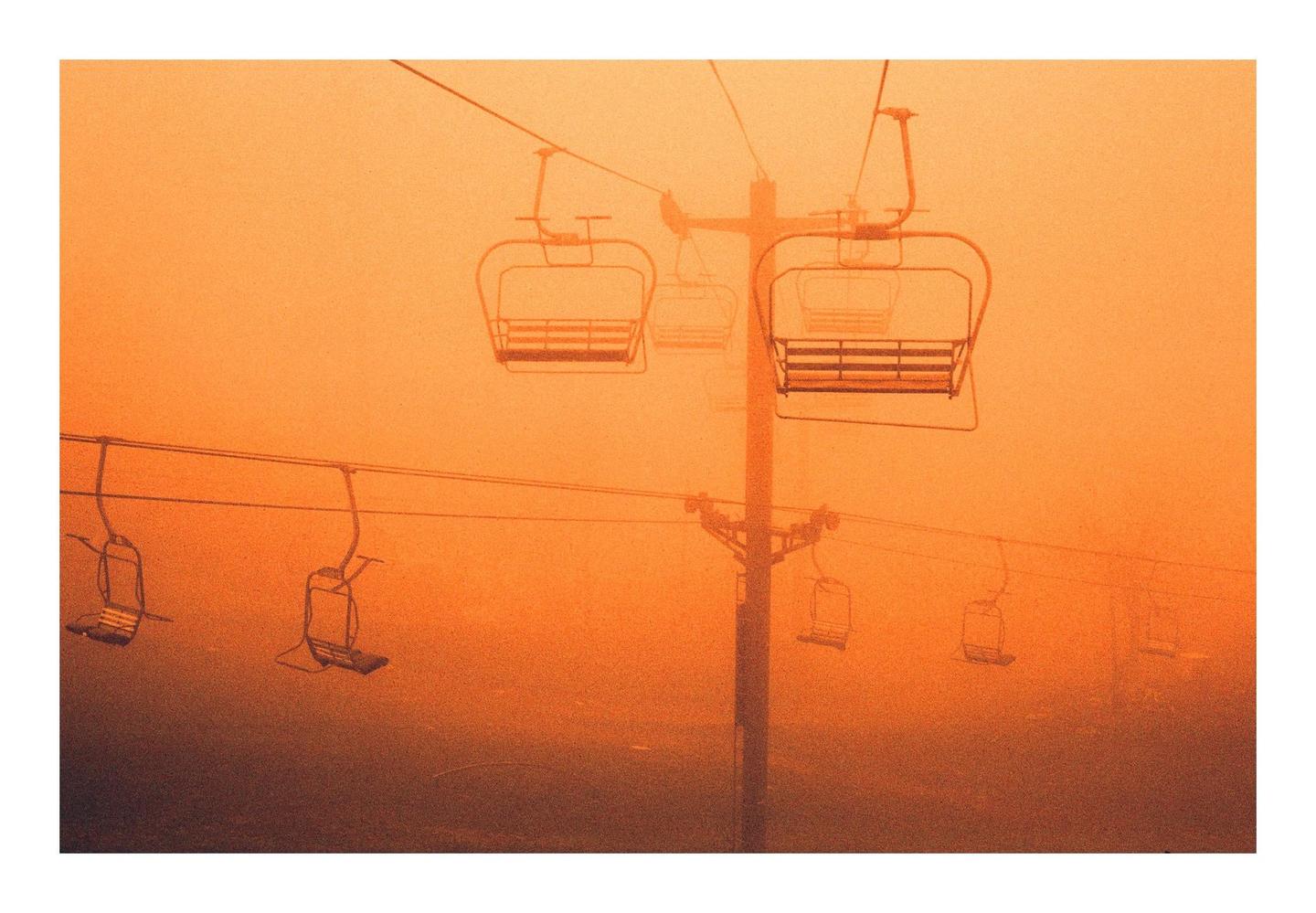 A ski lift with multiple chairs is visible against an orange, hazy sky.