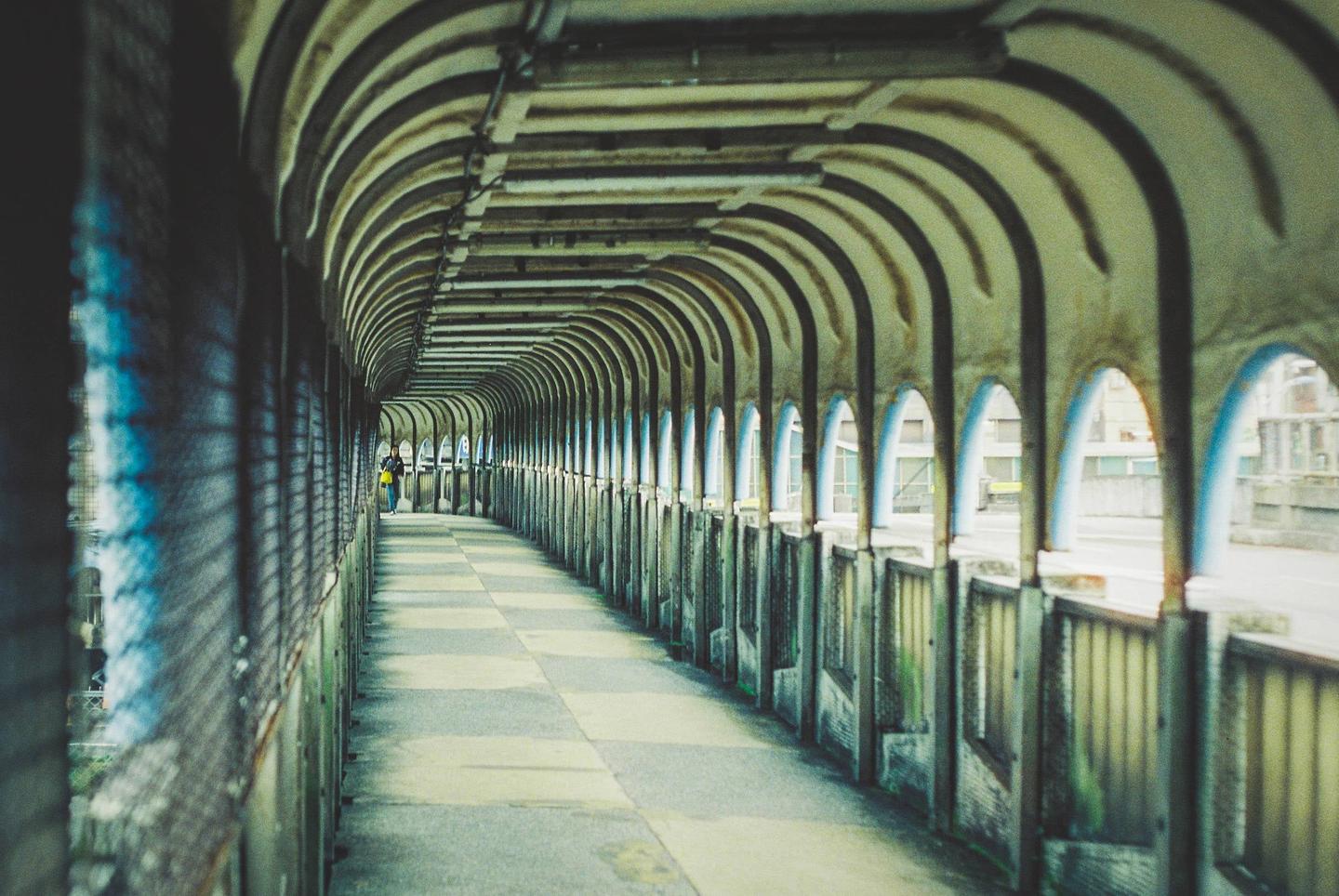 A person walks down a long, arched pedestrian bridge with a checkered floor.