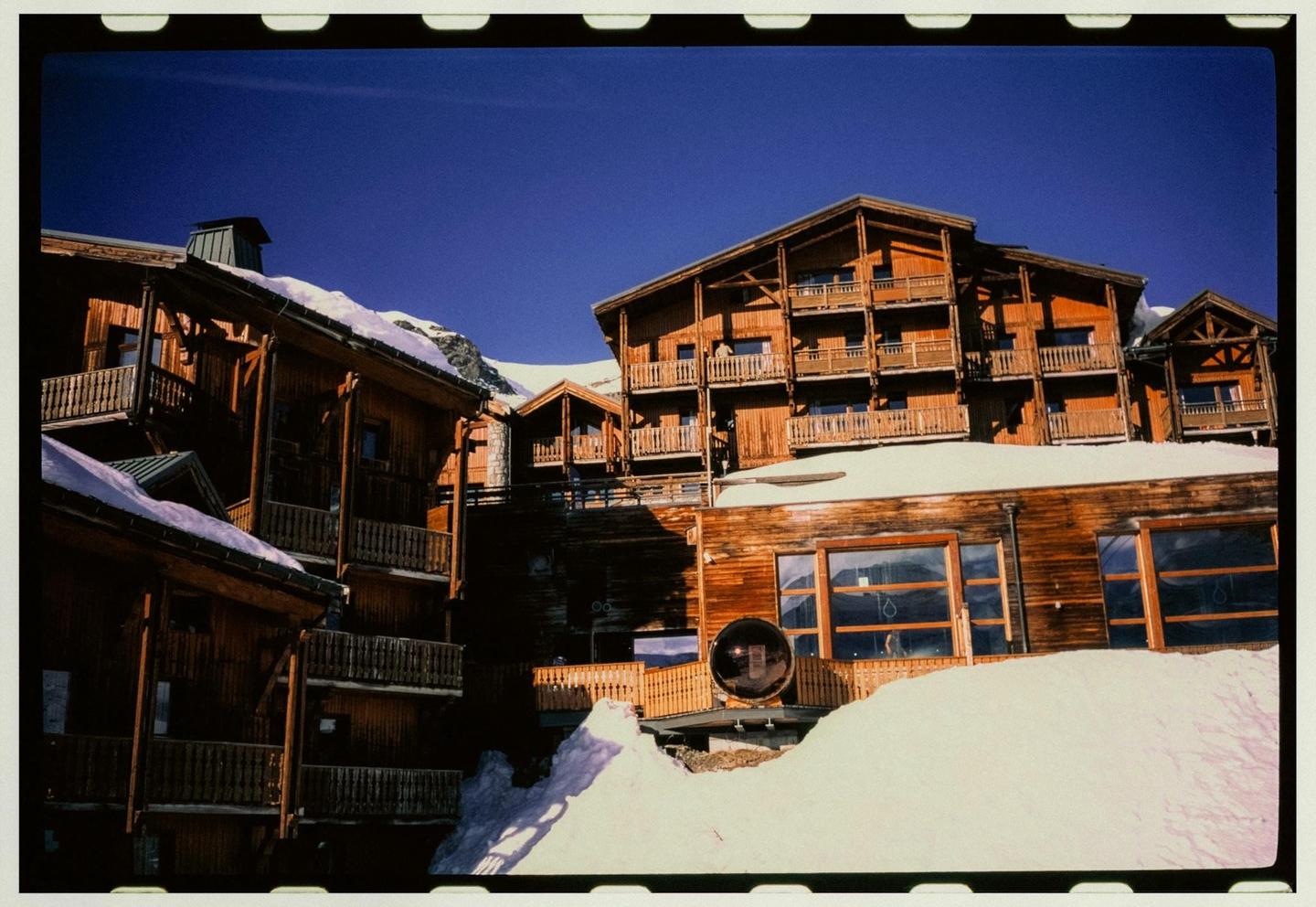A large wooden building with multiple balconies is covered in snow under a clear blue sky.