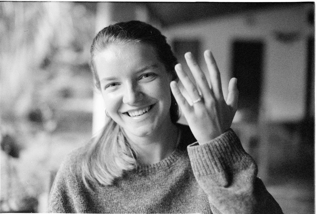 A woman smiles at the camera while showing a ring on her left hand.