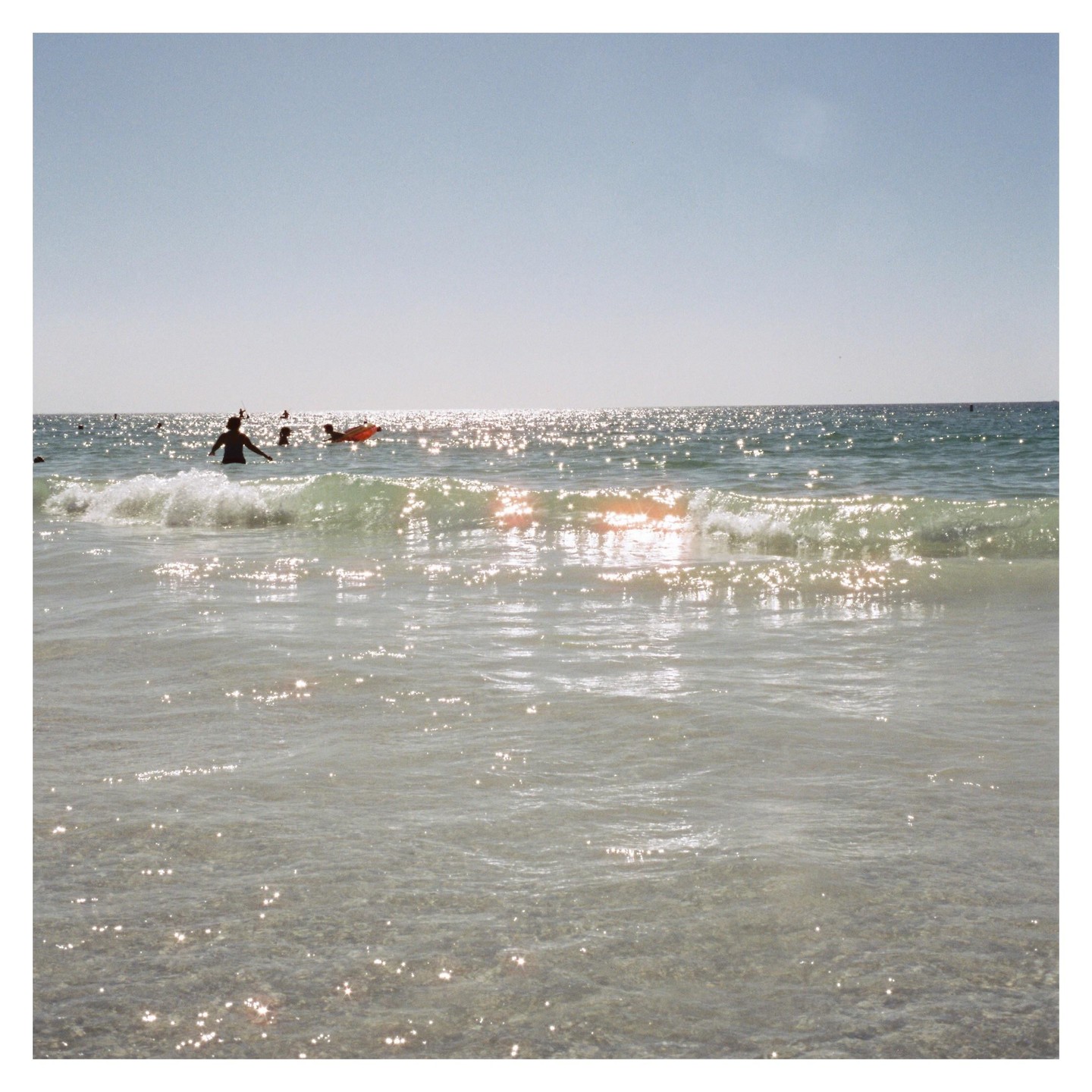 People swim in the ocean with sunlight reflecting on the water.