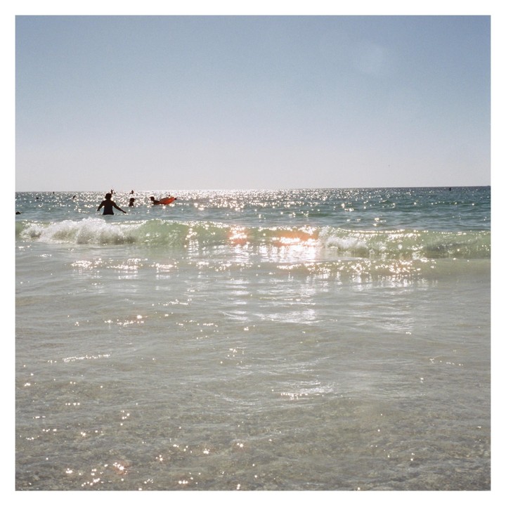 People swim in the ocean with sunlight reflecting on the water.