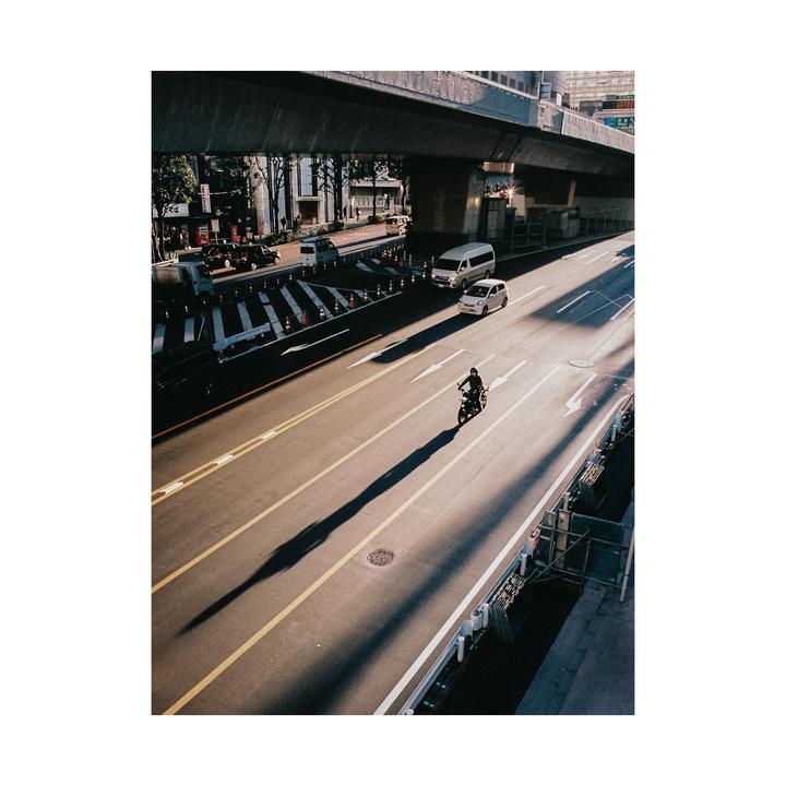 A person rides a motorcycle on a city street with an overpass above.