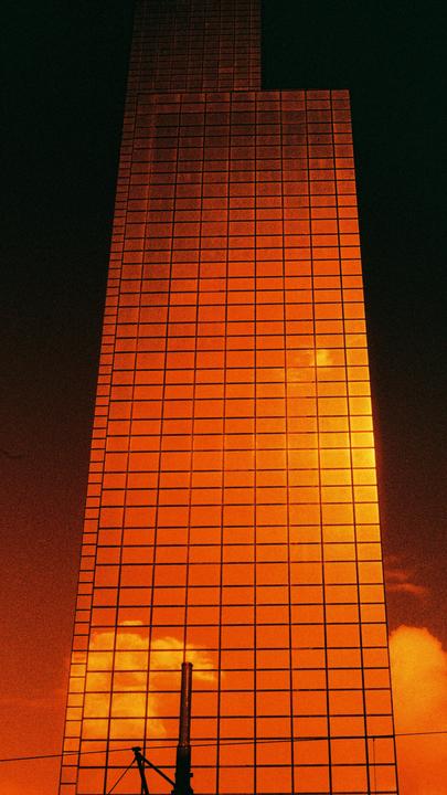 A tall building with orange-tinted windows reflects clouds against a dark sky.