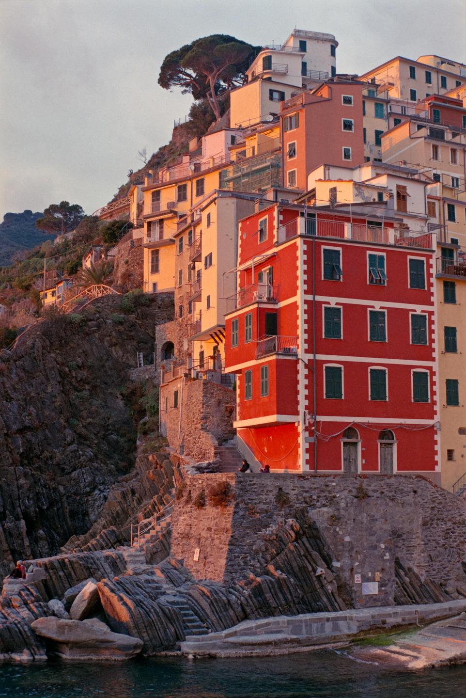 Colorful buildings are built into a steep cliffside above the water.