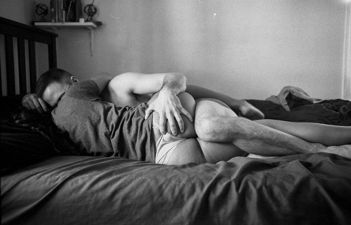 A couple lies intertwined on a bed, with a man's hand on a woman's bottom.