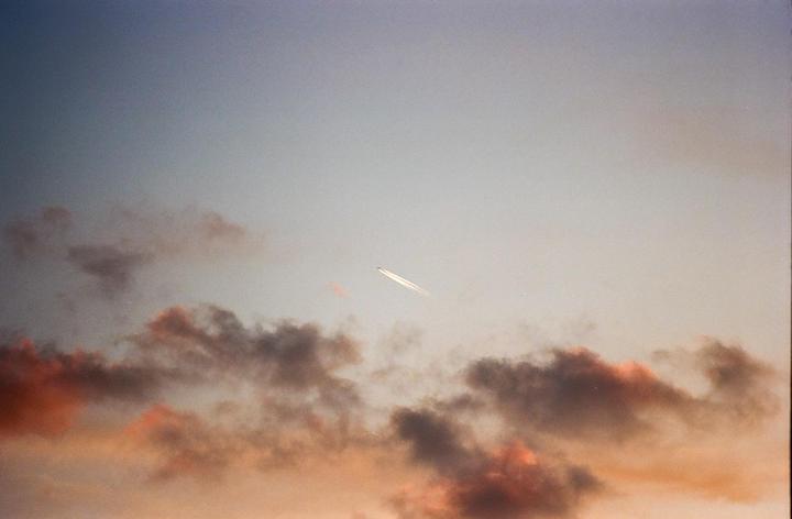 A jet airplane with a contrail flies across a sky with clouds at sunset.