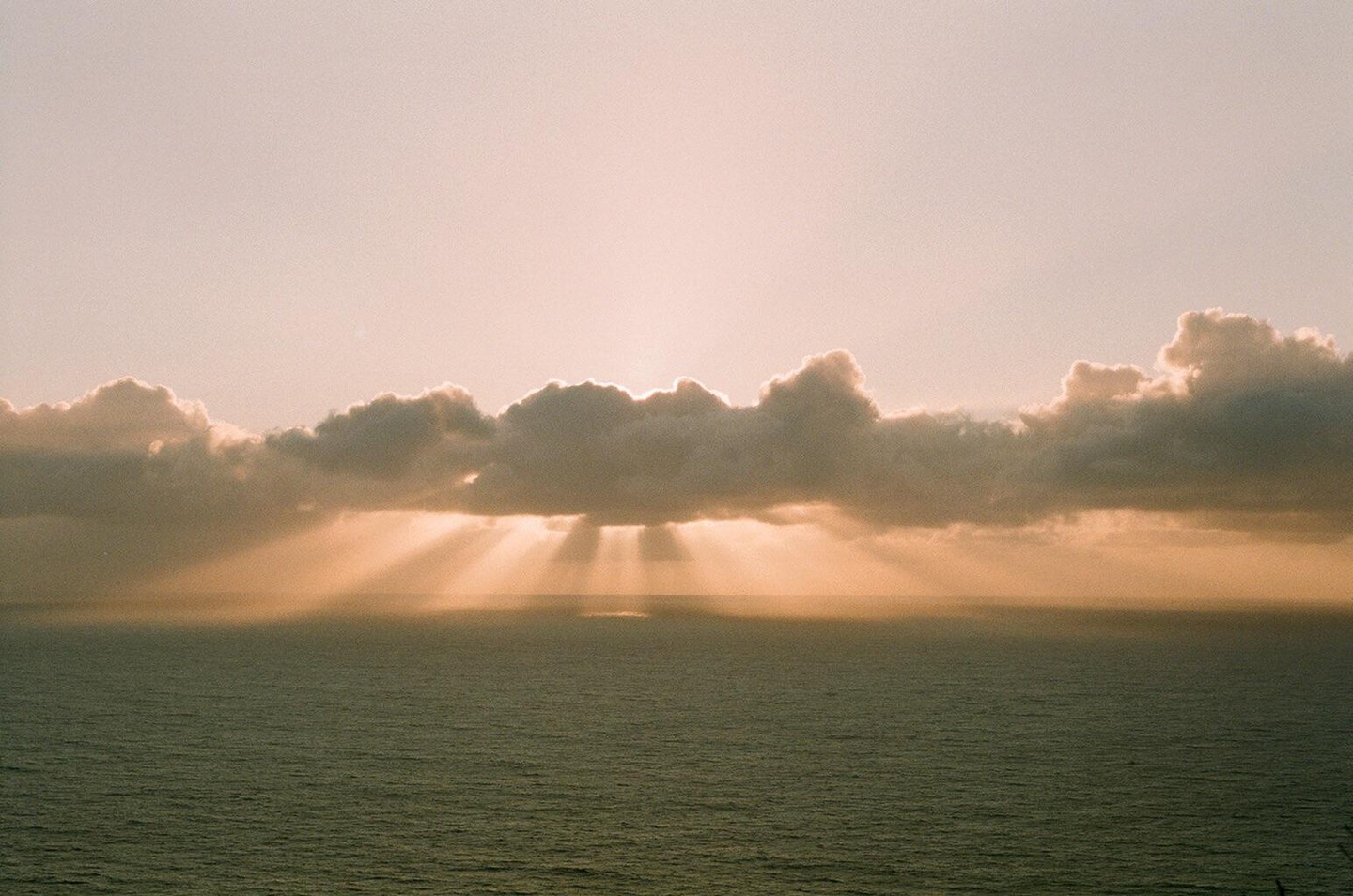 Sunlight streams through clouds over the ocean at sunset.