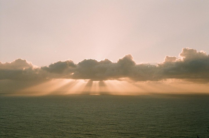 Sunlight streams through clouds over the ocean at sunset.