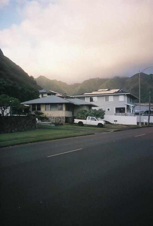 A street with houses and a white pickup truck is visible in front of a mountain range with low clouds.
