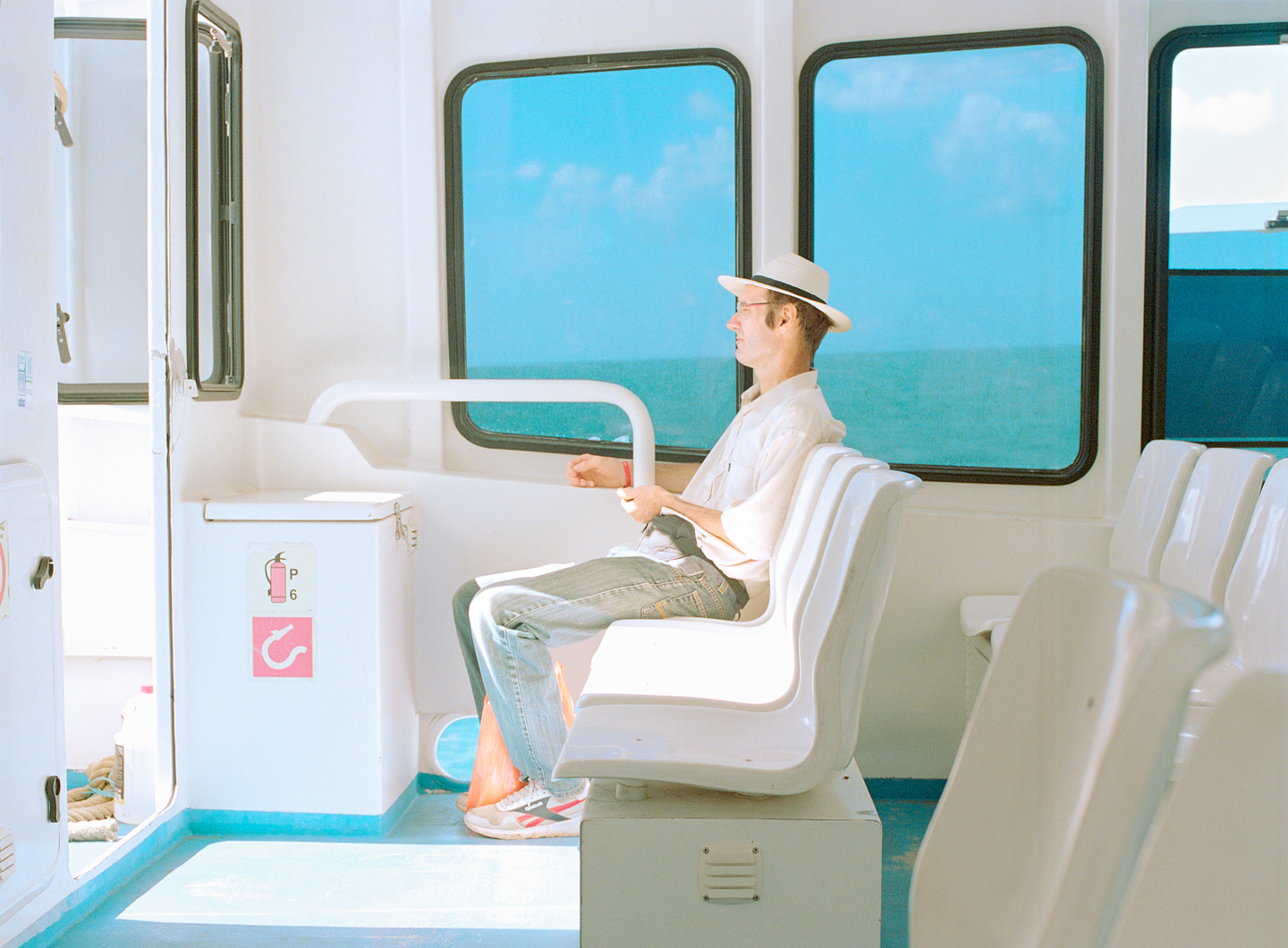 A man wearing a hat sits on a boat looking out a window at the ocean.