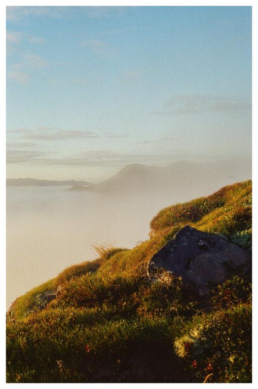 A rocky, grassy hillside overlooks a misty valley with mountains in the distance.