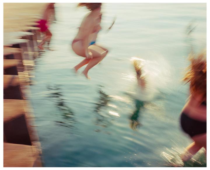 Several people jump into the water from a wooden dock, creating splashes.