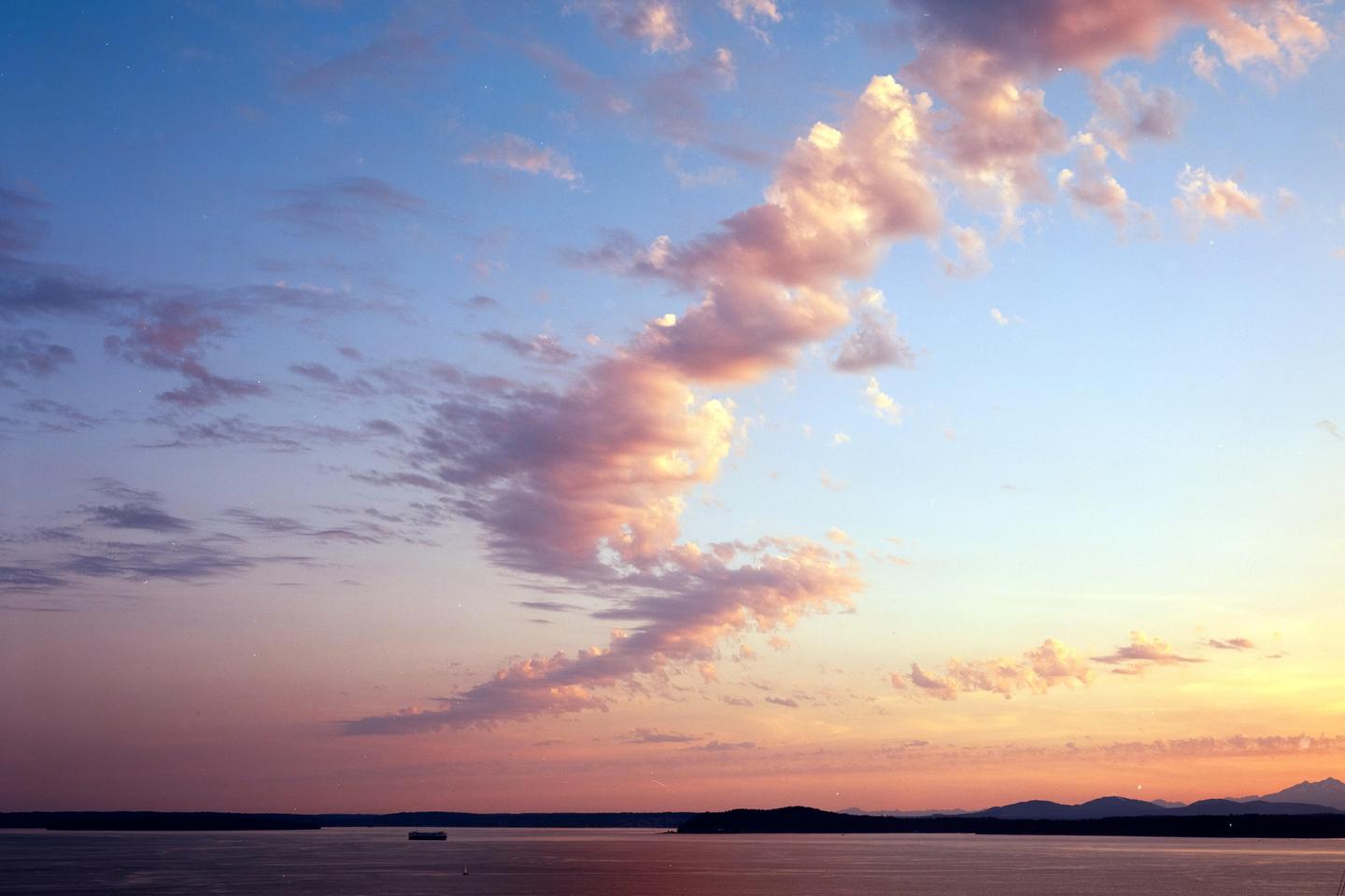 Pink and orange clouds stretch across a blue sky over a body of water with distant land and mountains.