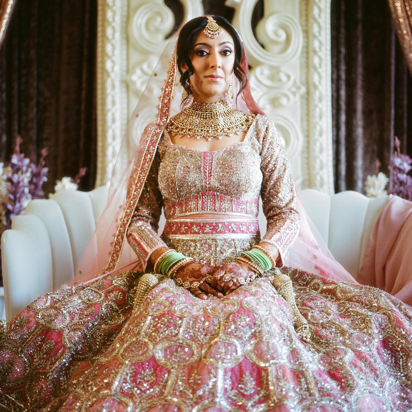A woman in a traditional wedding dress and jewelry sits on a white sofa.