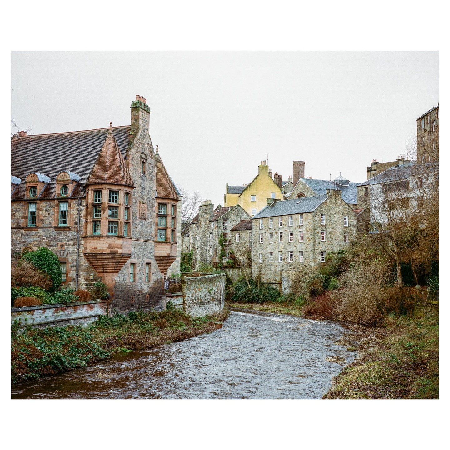 A river flows past old stone buildings with a large, ornate building on the left.