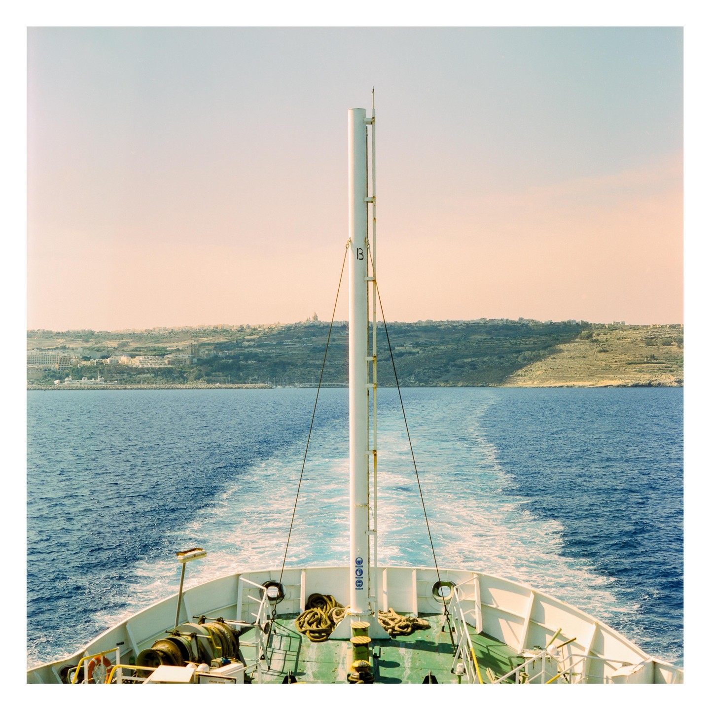 A ferry leaves a white wake on blue water, with a distant town on a hill under a pale sky.