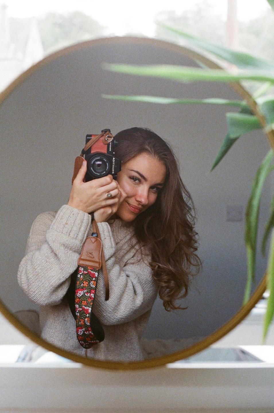 A woman holds a camera to her face while looking into a round mirror.