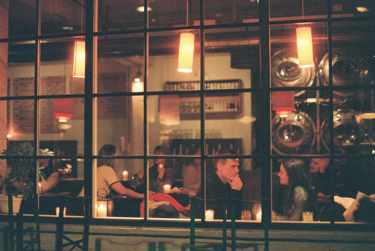 People are visible through a window with a grid of dark frames, illuminated by warm indoor lighting.