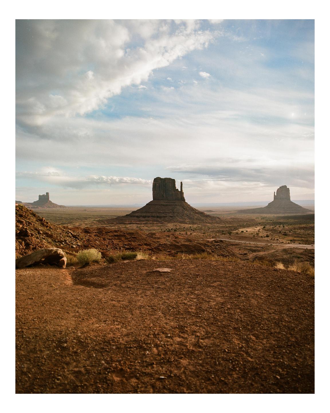 A wide shot shows three large rock formations in a desert landscape under a cloudy sky.