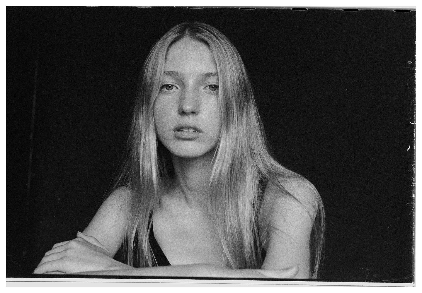 A young woman with long, straight hair looks directly at the viewer with her arms crossed in front of her.