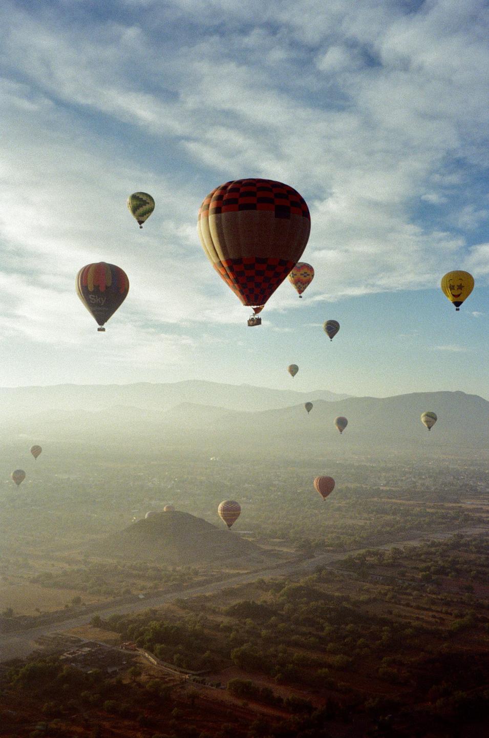 Hot air balloons float above a hazy landscape with mountains in the distance.