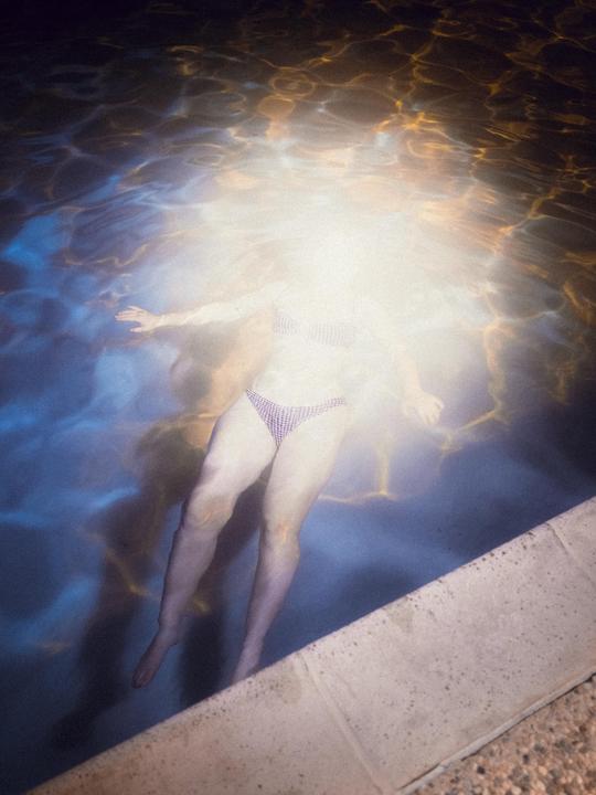 A woman floats in a swimming pool at night, illuminated by a bright light.