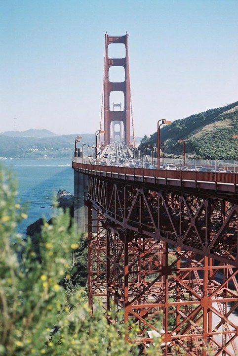 The Golden Gate Bridge is visible from a high angle, with cars driving across it and a body of water to the left.