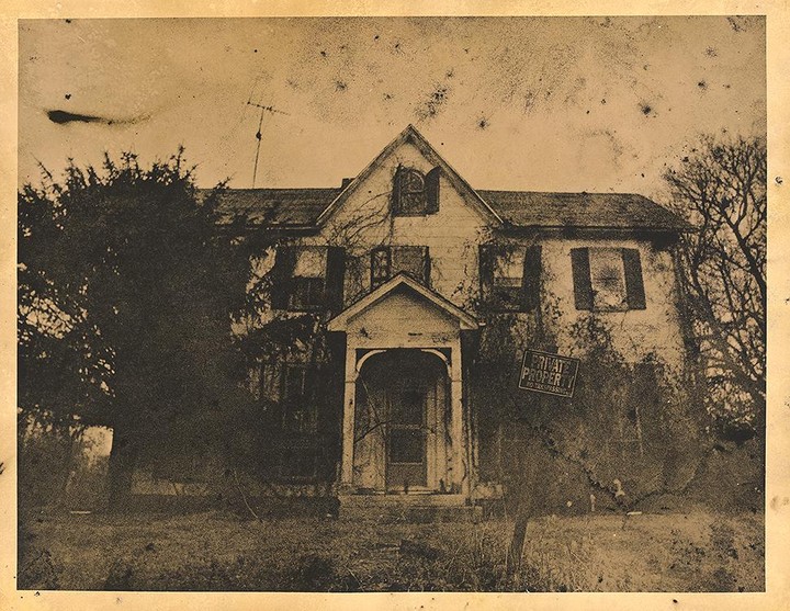 An old, dilapidated house with a "Private Property" sign on the front is surrounded by overgrown trees and grass.
