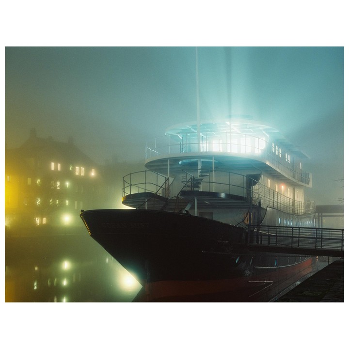 A large boat named Ocean Mist is docked at night, illuminated by bright lights and surrounded by fog.